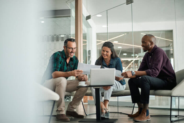 Three people sit around a table in an office, looking at documents and a laptop, engaged in a discussion about HOA Management in the DMV area.
